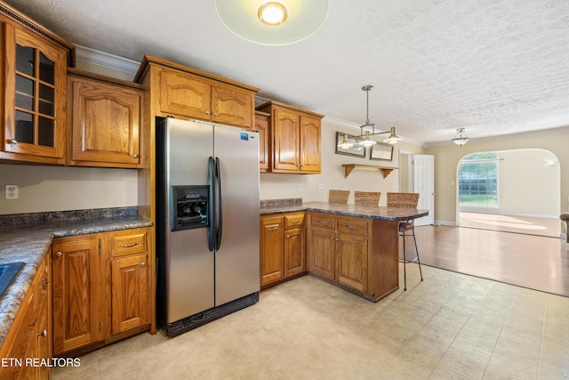 kitchen with a textured ceiling, brown cabinets, a peninsula, ornamental molding, and stainless steel refrigerator with ice dispenser