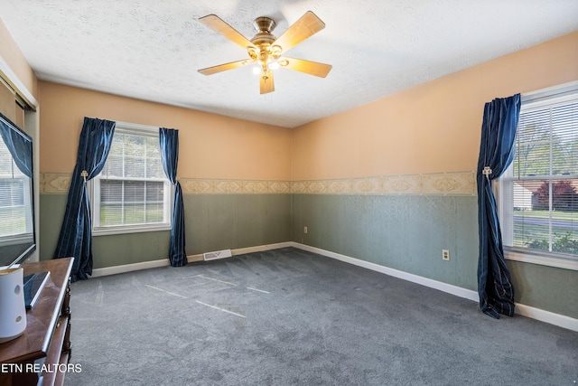 carpeted spare room featuring wainscoting, baseboards, a textured ceiling, and ceiling fan