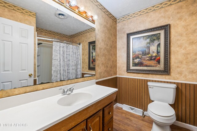 full bathroom featuring wood finished floors, visible vents, toilet, wainscoting, and a textured ceiling