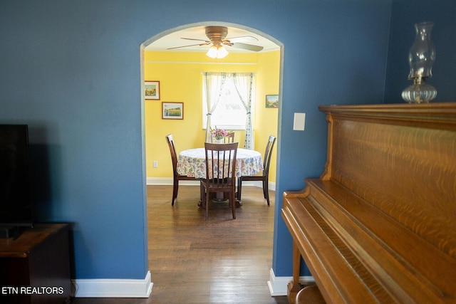 dining area with baseboards, arched walkways, ceiling fan, and dark wood-style floors
