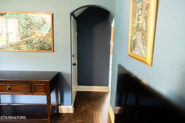 hall with baseboards, arched walkways, and wood finished floors