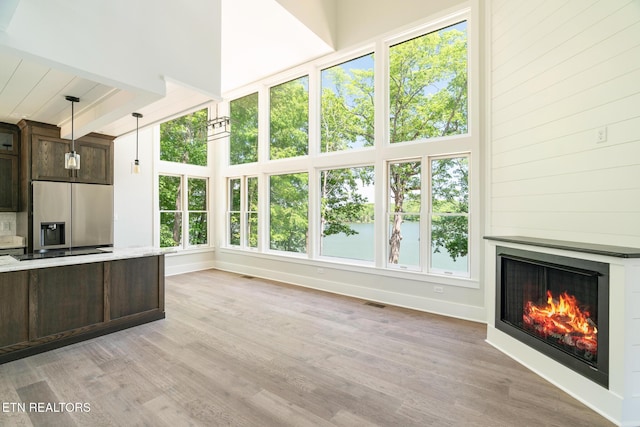 unfurnished living room with beamed ceiling, baseboards, a lit fireplace, and light wood-style flooring