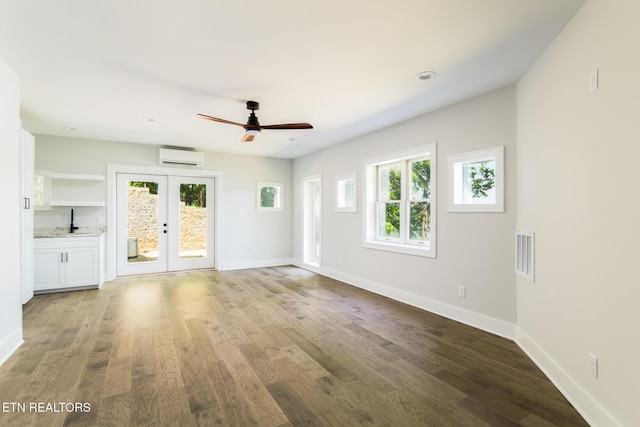 unfurnished living room with a wall mounted AC, a wealth of natural light, french doors, and visible vents