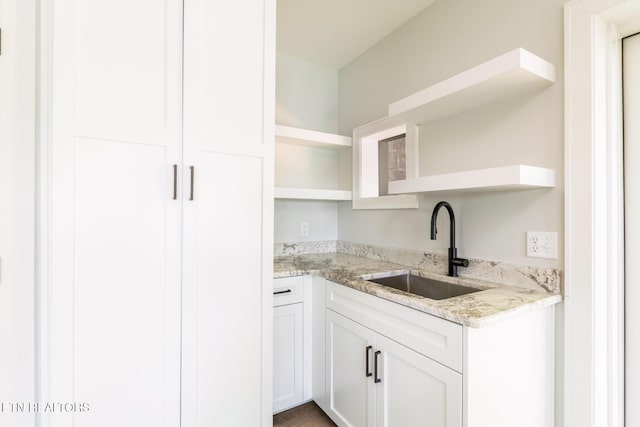 kitchen with a sink, light stone counters, white cabinets, and open shelves
