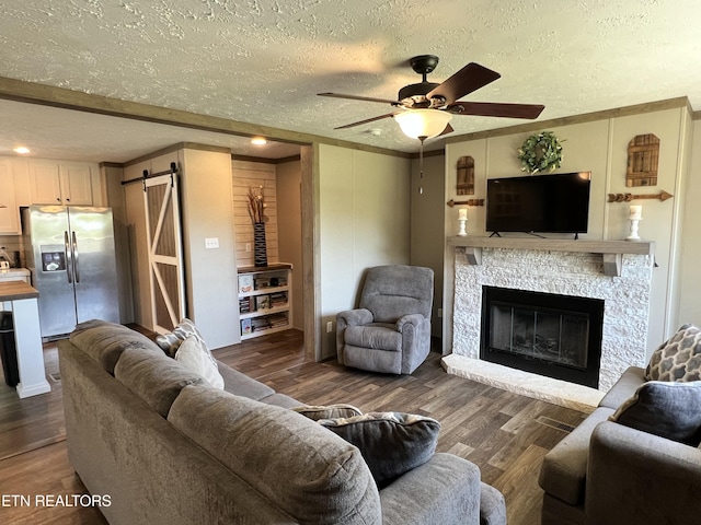 534 Wiggins Rd, Tellico Plains, TN 37385 - living area featuring a barn door, wood finished floors, a ceiling fan, a glass covered fireplace, and a textured ceiling