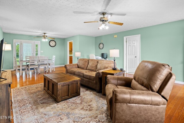 living room with a textured ceiling, ceiling fan, baseboards, and light wood-style floors