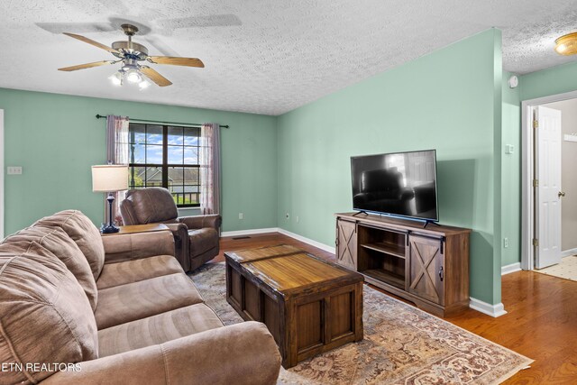 living room with a textured ceiling, a ceiling fan, wood finished floors, and baseboards