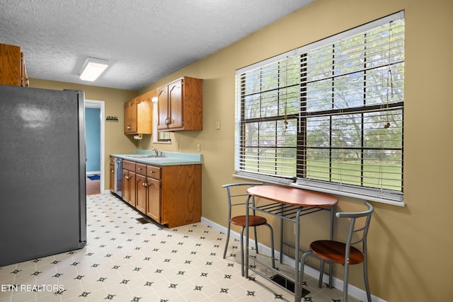 kitchen with appliances with stainless steel finishes, light countertops, brown cabinets, a sink, and baseboards