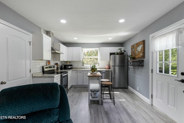 kitchen featuring decorative backsplash, appliances with stainless steel finishes, light countertops, light wood-type flooring, and wall chimney exhaust hood