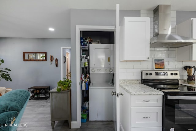 kitchen with wall chimney range hood, decorative backsplash, stacked washer / dryer, white cabinets, and electric stove