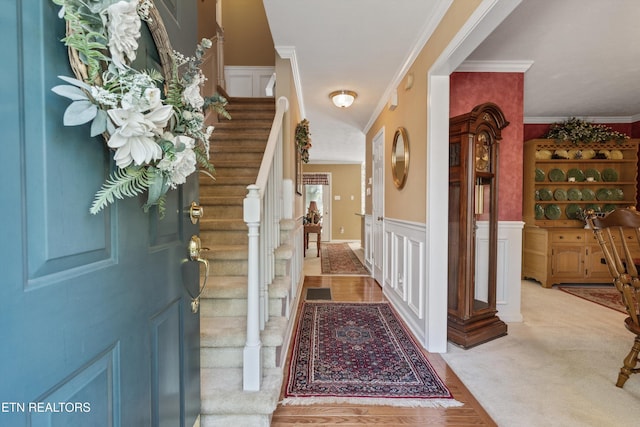 entrance foyer with crown molding, wainscoting, stairway, and a decorative wall