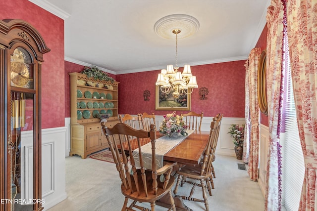 dining space with a wainscoted wall, ornamental molding, a chandelier, and light colored carpet