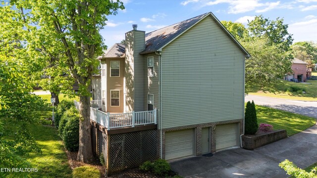 view of property exterior featuring an attached garage, a wooden deck, driveway, and a chimney