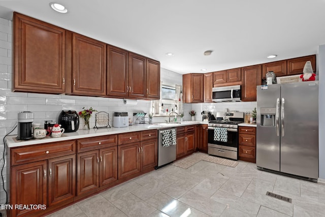 kitchen with stainless steel appliances, a sink, visible vents, backsplash, and light countertops