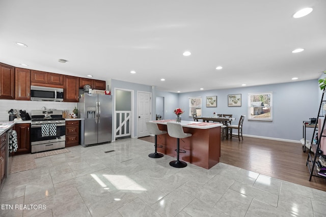 kitchen with a kitchen breakfast bar, light countertops, backsplash, baseboards, and appliances with stainless steel finishes