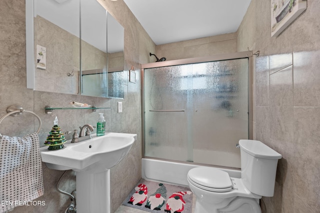 bathroom featuring toilet, bath / shower combo with glass door, and tile walls
