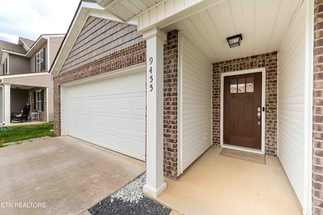 property entrance with an attached garage, driveway, and brick siding