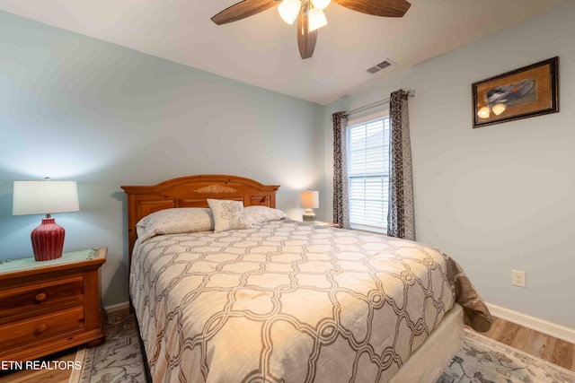 bedroom with a ceiling fan, baseboards, visible vents, and wood finished floors