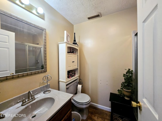 bathroom with a shower with shower door, toilet, visible vents, wood finished floors, and vanity