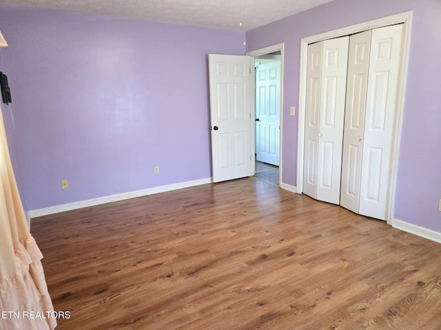 unfurnished bedroom featuring baseboards, wood finished floors, and a closet