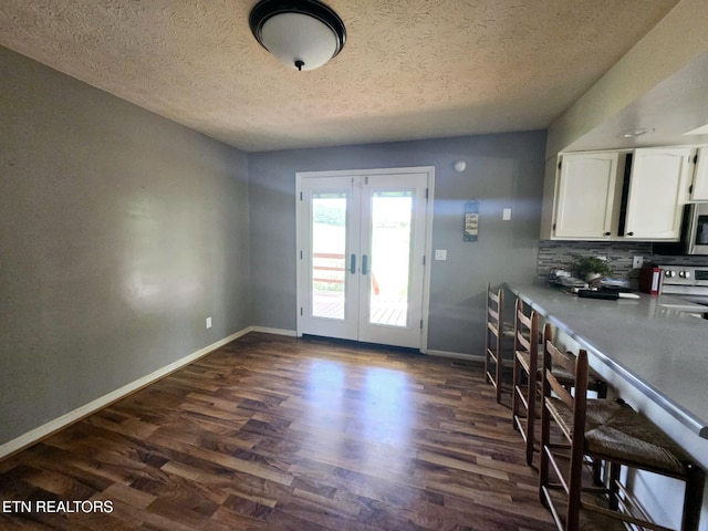 interior space featuring french doors, baseboards, a textured ceiling, and dark wood finished floors