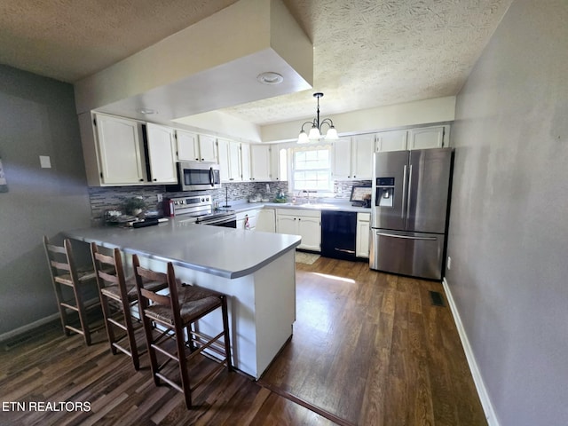 kitchen with stainless steel appliances, a textured ceiling, a chandelier, and dark wood-style flooring