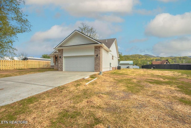 view of side of home with driveway, fence, brick siding, an attached garage, and a lawn