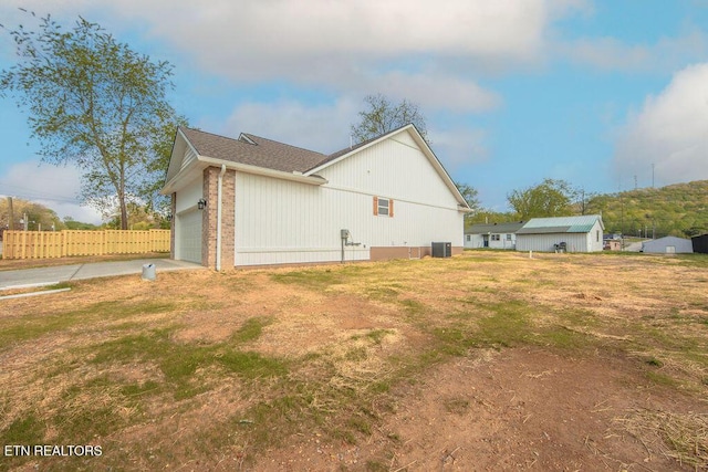 view of home's exterior with central air condition unit, concrete driveway, a shingled roof, an attached garage, and fence
