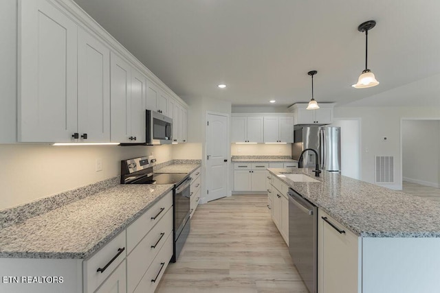 kitchen with white cabinets, recessed lighting, light wood finished floors, a sink, and appliances with stainless steel finishes