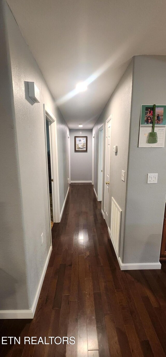 corridor with baseboards, dark wood-type flooring, and visible vents