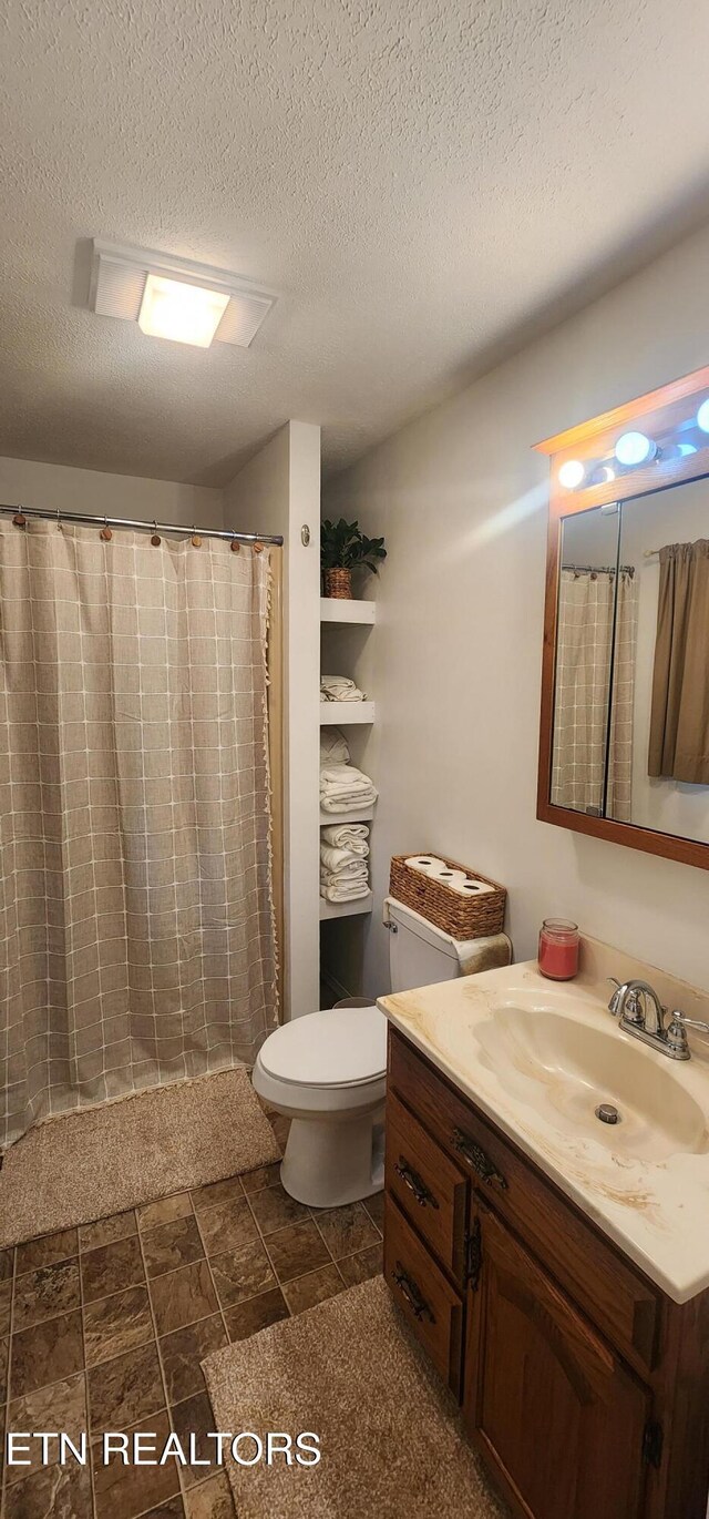 full bathroom with a textured ceiling, vanity, a shower with curtain, stone finish flooring, and toilet