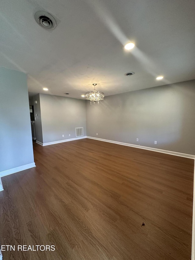 unfurnished room featuring dark wood-style floors, visible vents, baseboards, and an inviting chandelier