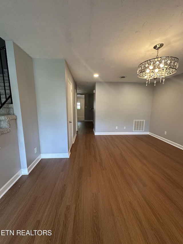 unfurnished living room with baseboards, visible vents, an inviting chandelier, and dark wood finished floors