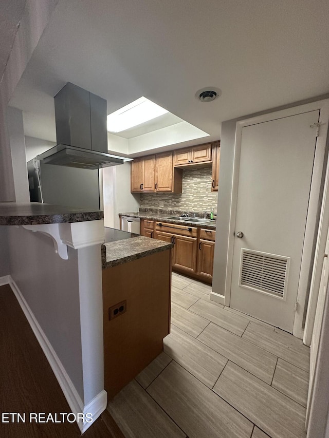 kitchen featuring visible vents, island range hood, a sink, tasteful backsplash, and wood finish floors