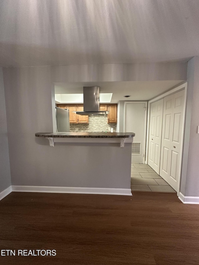 kitchen with island exhaust hood, freestanding refrigerator, baseboards, visible vents, and decorative backsplash