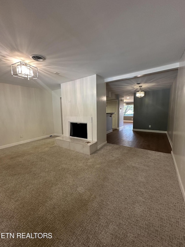 unfurnished living room with dark colored carpet, a tiled fireplace, visible vents, baseboards, and a chandelier