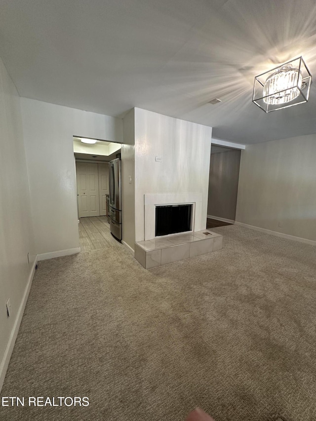 unfurnished living room featuring light colored carpet, baseboards, and a tiled fireplace