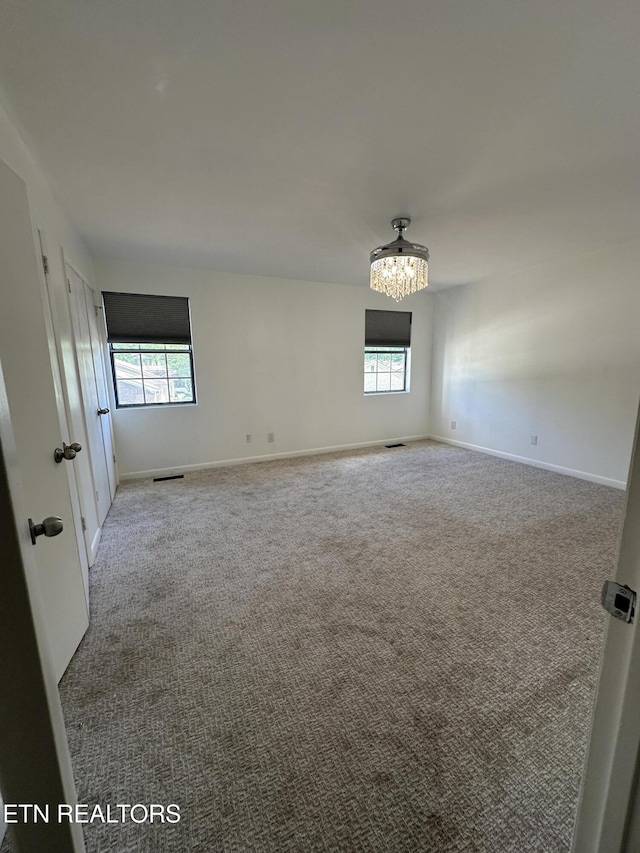 unfurnished room with plenty of natural light, carpet flooring, and a notable chandelier