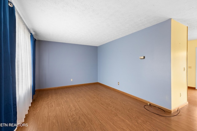 spare room featuring baseboards, wood finished floors, and a textured ceiling