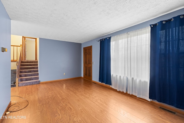 unfurnished living room featuring a textured ceiling, visible vents, baseboards, wood finished floors, and stairs