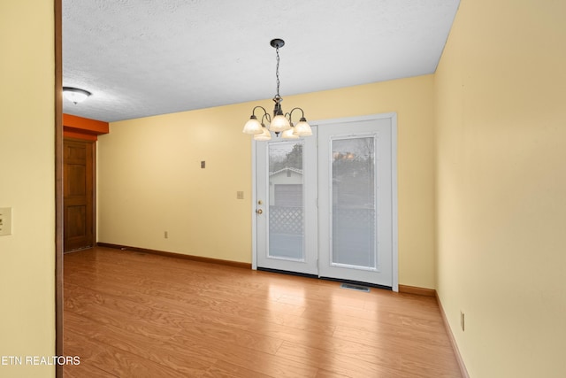 unfurnished room with baseboards, a notable chandelier, wood finished floors, and visible vents