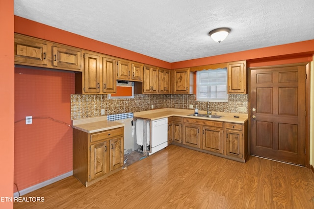 kitchen with brown cabinets, light countertops, a sink, white dishwasher, and light wood-style flooring