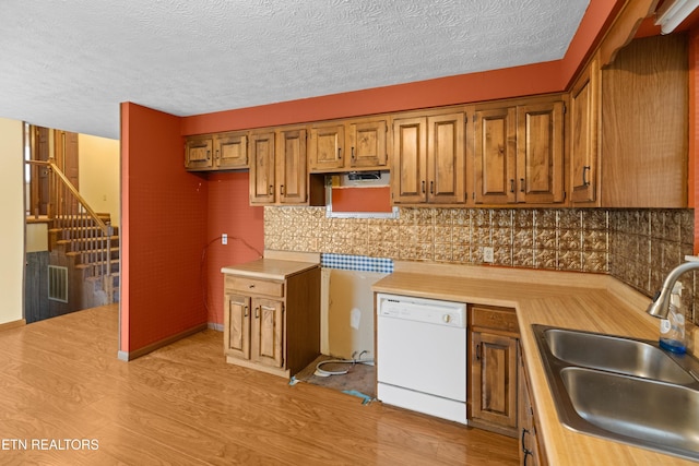 kitchen with decorative backsplash, white dishwasher, light countertops, and a sink