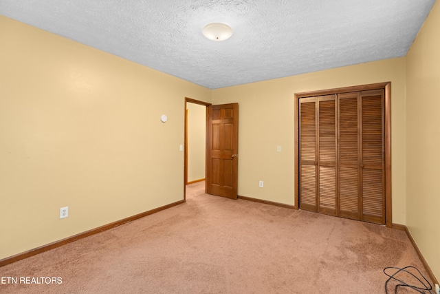 unfurnished bedroom with baseboards, light carpet, a textured ceiling, and a closet