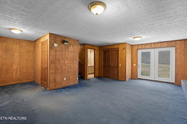 unfurnished living room featuring stairway, wood walls, a textured ceiling, and carpet