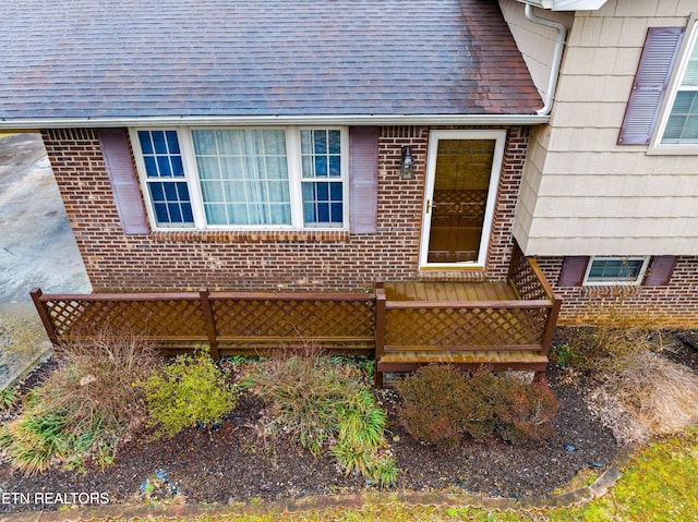 doorway to property with brick siding and roof with shingles