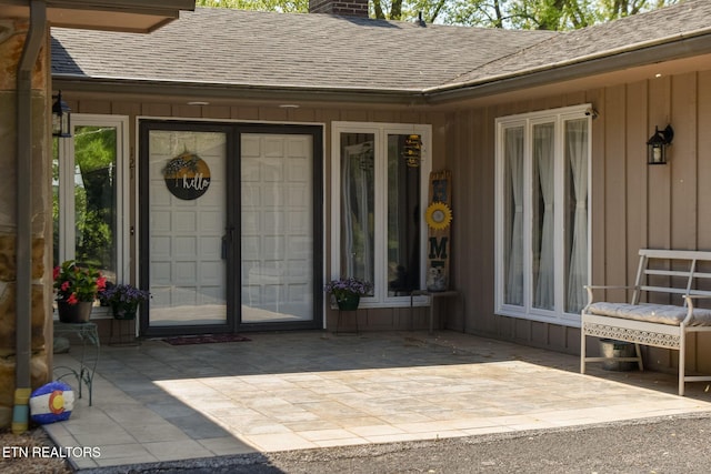 doorway to property featuring a chimney, board and batten siding, a patio area, and roof with shingles