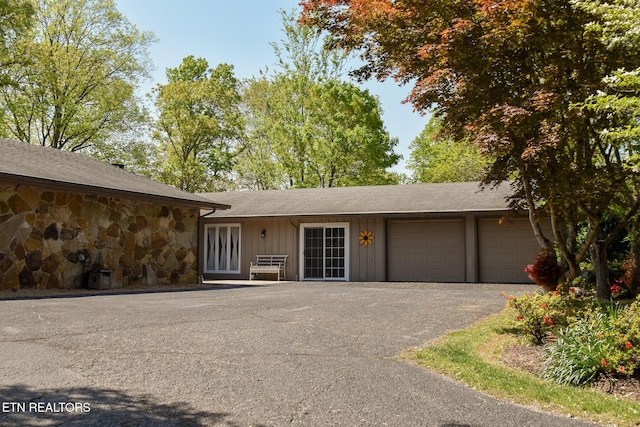 ranch-style house featuring a garage, roof with shingles, aphalt driveway, and stone siding