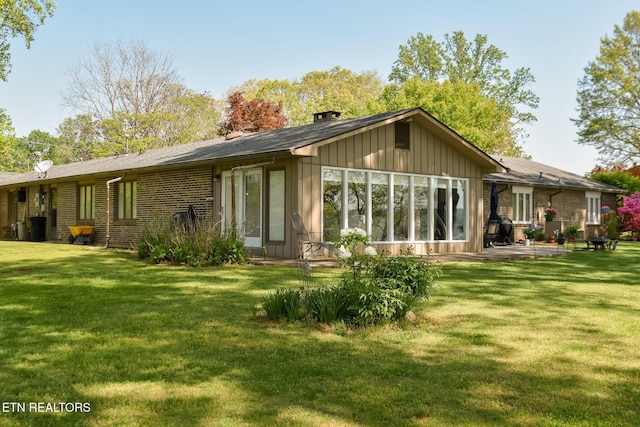 rear view of property with a chimney, brick siding, a patio area, and a lawn