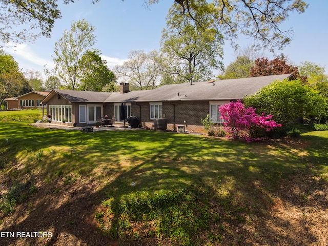rear view of house featuring a patio, a chimney, a yard, central AC unit, and brick siding